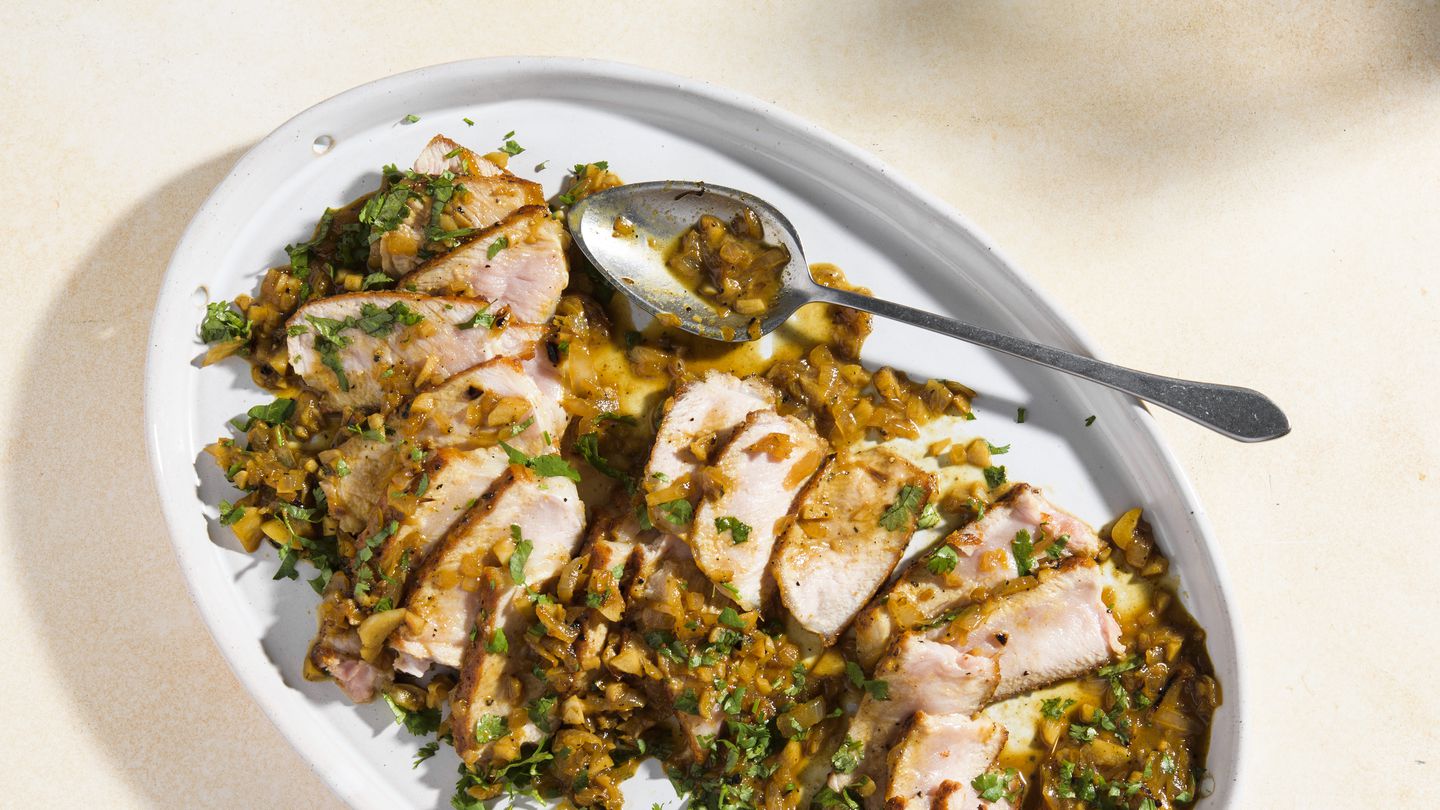 An oval serving platter holding sliced pork topped with a dark sauce and garnished with green herbs.