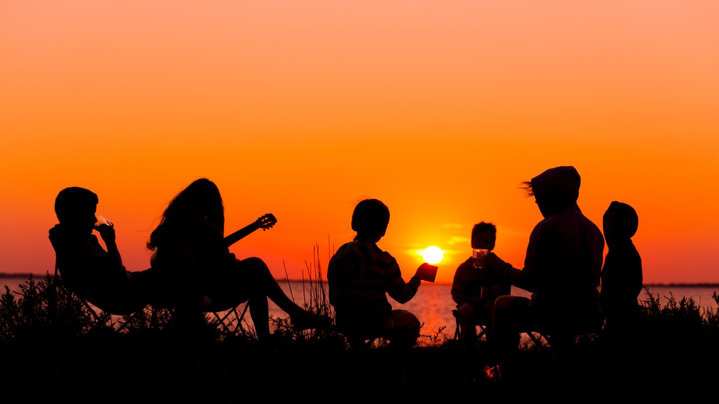 Silhouette of group of people sitting on the beach with campfire at sunset