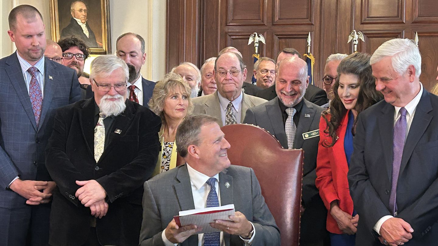 Lawmakers look on as New Hampshire Governor Chris Sununu signs a $15 billion state budget.