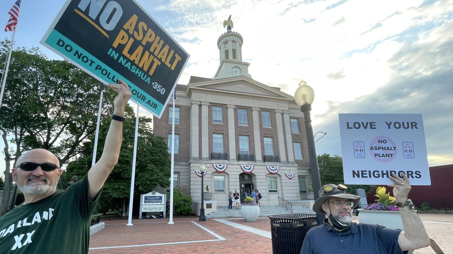 Paul Pederzani, left, and Doug Wilcox, right, hold signs outside City Hall in Nashua on June 15 to oppose the proposed construction of an asphalt plant in a central part of the city. Later that evening, after months of consideration, the city's Planning Board rejected the proposal.
