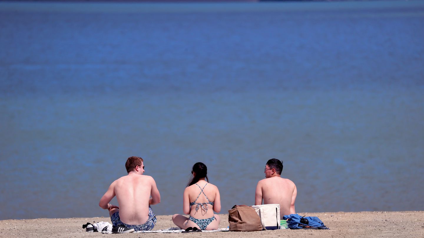 Three people soak up sun at Carson Beach in South Boston.