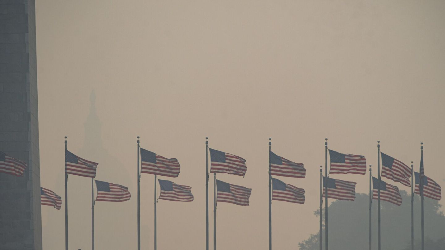 Visitors walk past American flags at the Washington Monument shrouded in smoke from Canada wildfires in Washington on Thursday.